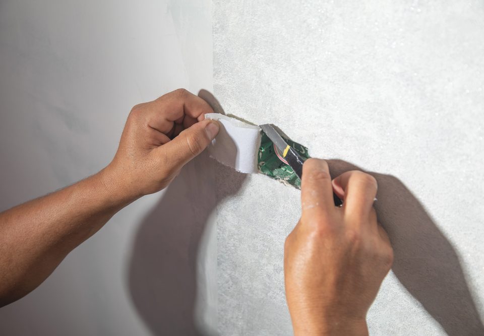 Worker cutting wallpaper near socket box to the wall.