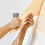 Man in with a scraper in the process of removing old wallpaper.
